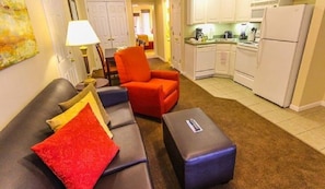 Cozy living space with a sofa, ottoman, and armchair, featuring a compact kitchen area with cabinetry and appliances.