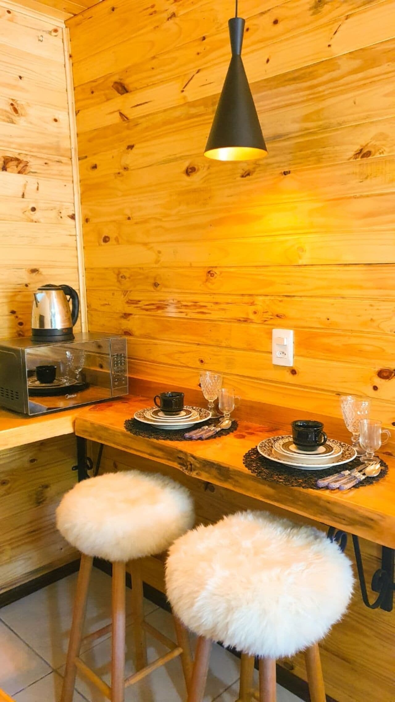 Interior de madera con cocina, que incluye microondas, hervidor y taburetes de bar.