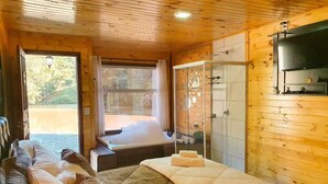 A wooden cabin bedroom with a large bed, a separate sleeping area, a glass shower, and a view of a natural landscape. - Cabana Brisa Serrana - Urubici-SC (Urubici)