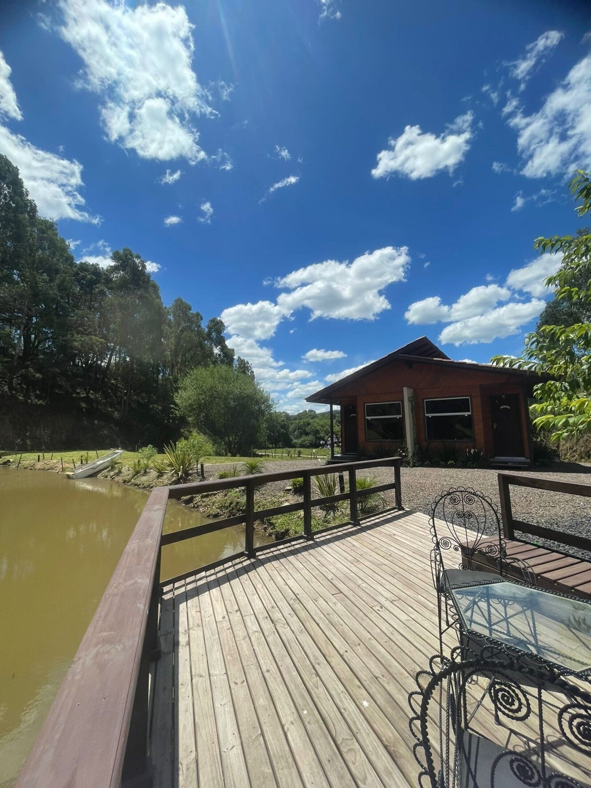 A wooden deck with a metal railing overlooking a body of water, a small pavilion, and a clear blue sky with scattered clouds.