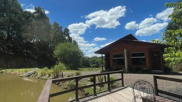 A wooden deck with a metal railing overlooking a body of water, a small pavilion, and a clear blue sky with scattered clouds.