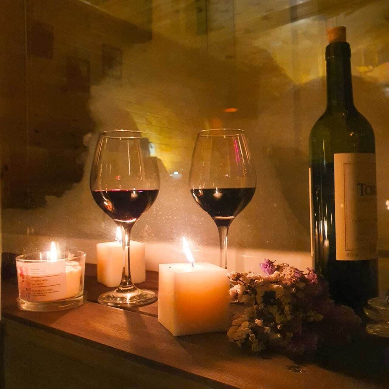 Una mesa con dos copas de vino, una vela, una botella de vino y un candelabro con flores.