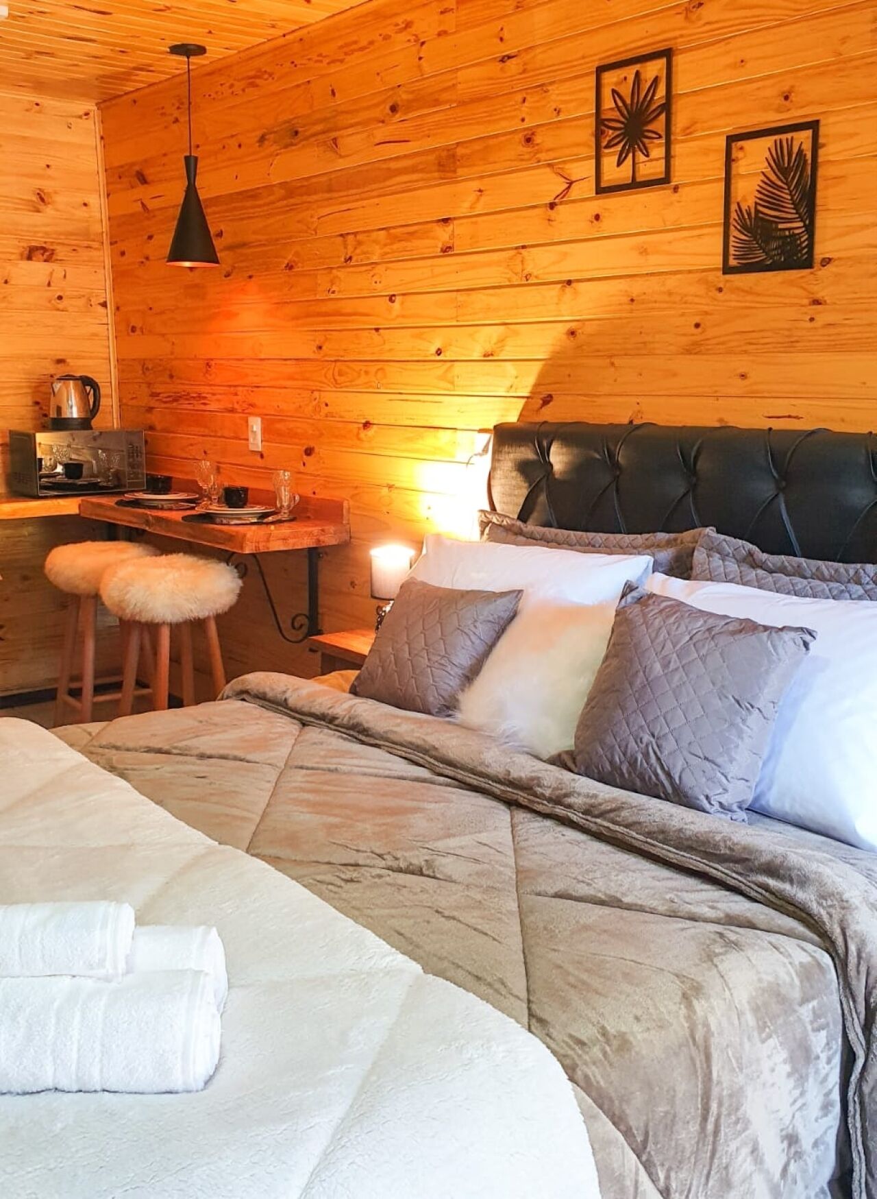 A cozy wooden cabin room with a bed, a small table with a kettle, and a chair.