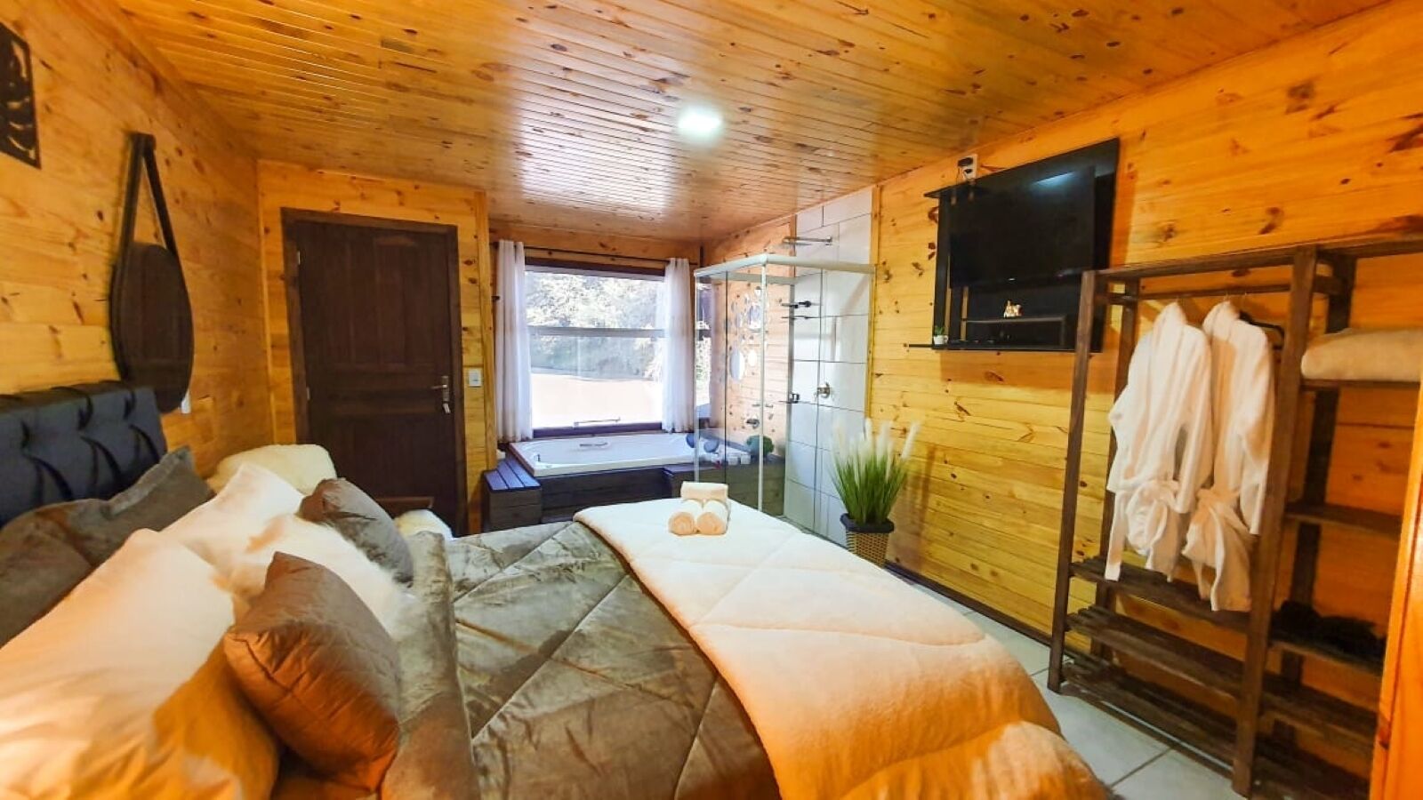 A cozy wooden cabin room with a bed, a TV, and a rack with towels.
