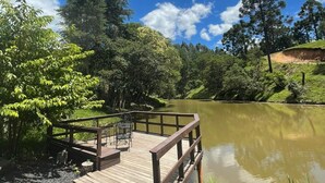 A wooden deck extending over a calm river, surrounded by lush greenery and trees. - Cabana Brisa Serrana - Urubici-SC (Urubici)
