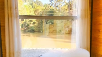 A wooden cabin with a large window, a bathtub filled with water, and a view of a forested area.