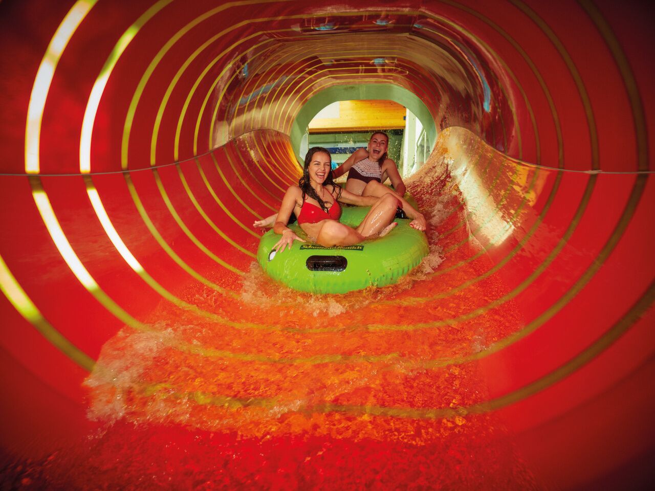 Uno scivolo acquatico con due persone all'interno di un tubo verde.