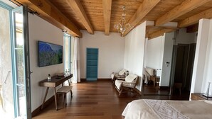 A spacious bedroom with wooden flooring, a large bed, a desk with a chair, a blue shelving unit, and a large mirror. - Antoine (Bonifacio)