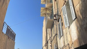 A view through an archway of a building with multiple balconies, some with umbrellas, and a clear blue sky above. - Antoine (Bonifacio)
