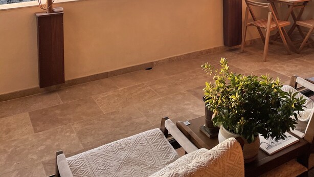 A balcony with a view of cliffs and sea, wooden furniture, and a potted plant. - Antoine (Bonifacio)