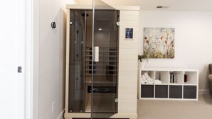 Habitació moderna amb una porta corredissa de vidre que dona a un armari, una prestatgeria amb llibres i tovalloles doblegades, i un quadre floral a la paret.