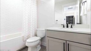 Un bany modern amb un vàter blanc, un mirall gran i un lavabo blanc.
