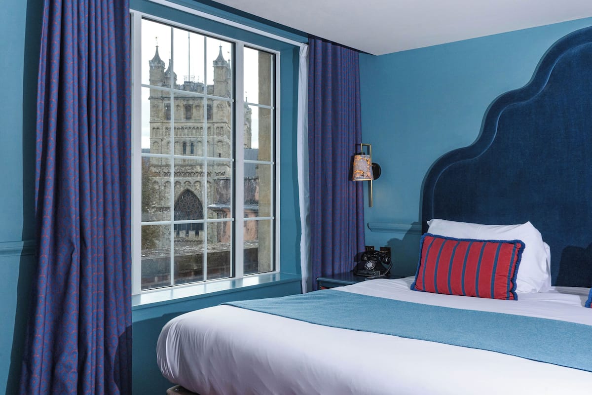 A hotel room with a large window, a bed with white and blue bedding, and a view of a historic building.