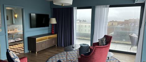 A modern living room with a red sofa, a red armchair, a round coffee table, a TV, and a large window with a city view.