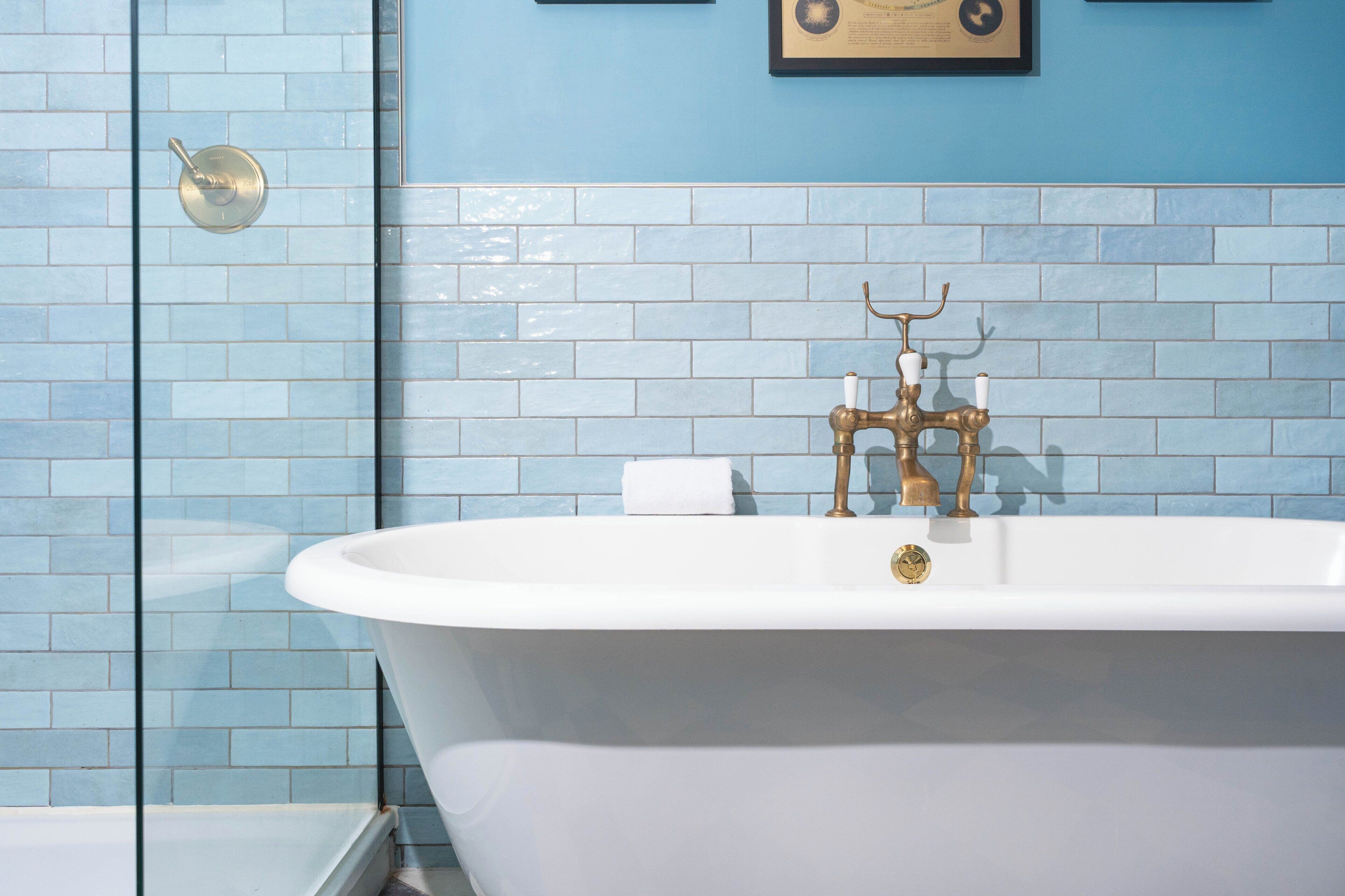 A bathroom with a white bathtub, a gold faucet, and blue-tiled walls.
