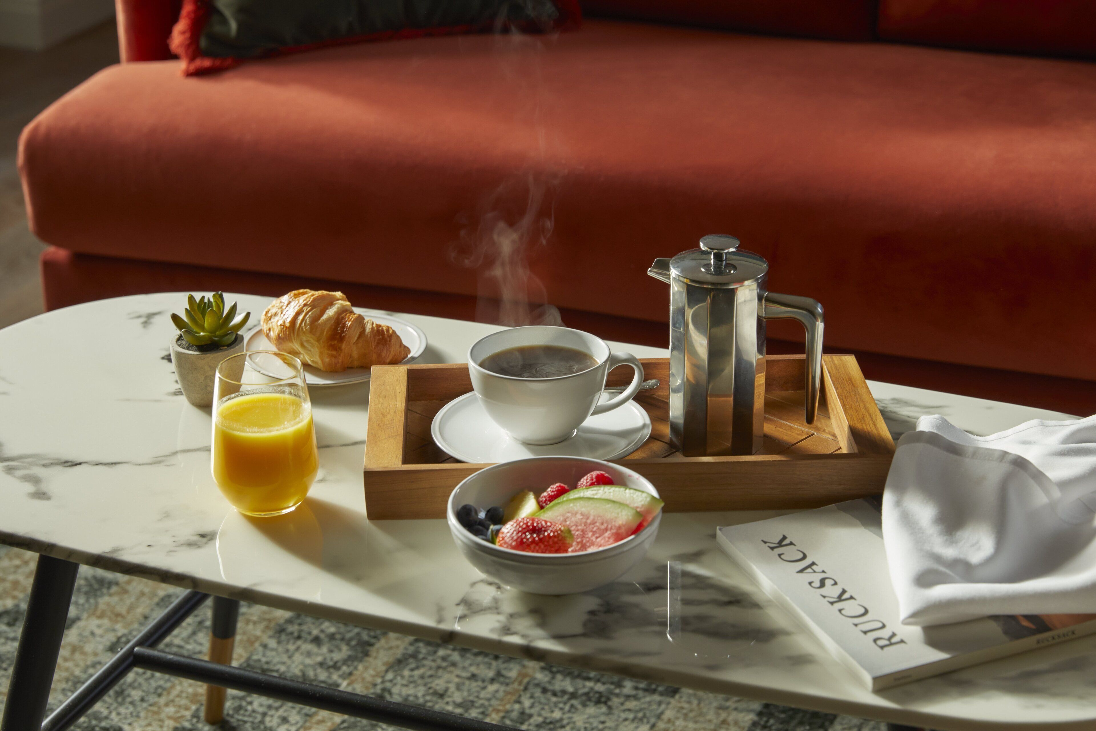 A breakfast setup on a marble table with a croissant, coffee, juice, and a fruit bowl.
