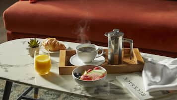 A breakfast setup on a marble table with a croissant, coffee, juice, and a fruit bowl.