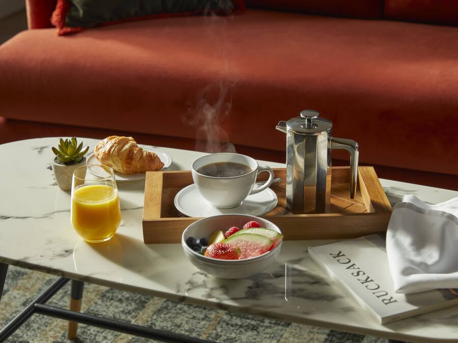 A breakfast setup on a marble table with a croissant, coffee, juice, and a fruit bowl.