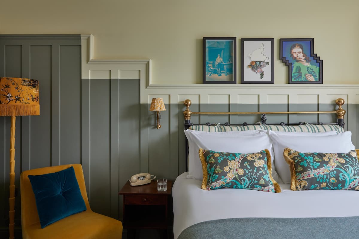 A neatly arranged hotel room with a bed, a chair, a nightstand with a lamp, and framed artwork on the wall.