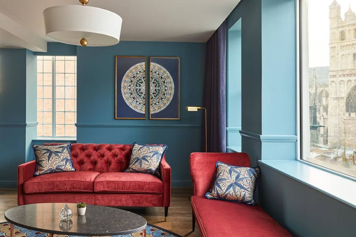 A room with a red sofa, a round table, and a large window with a view of a historic building.