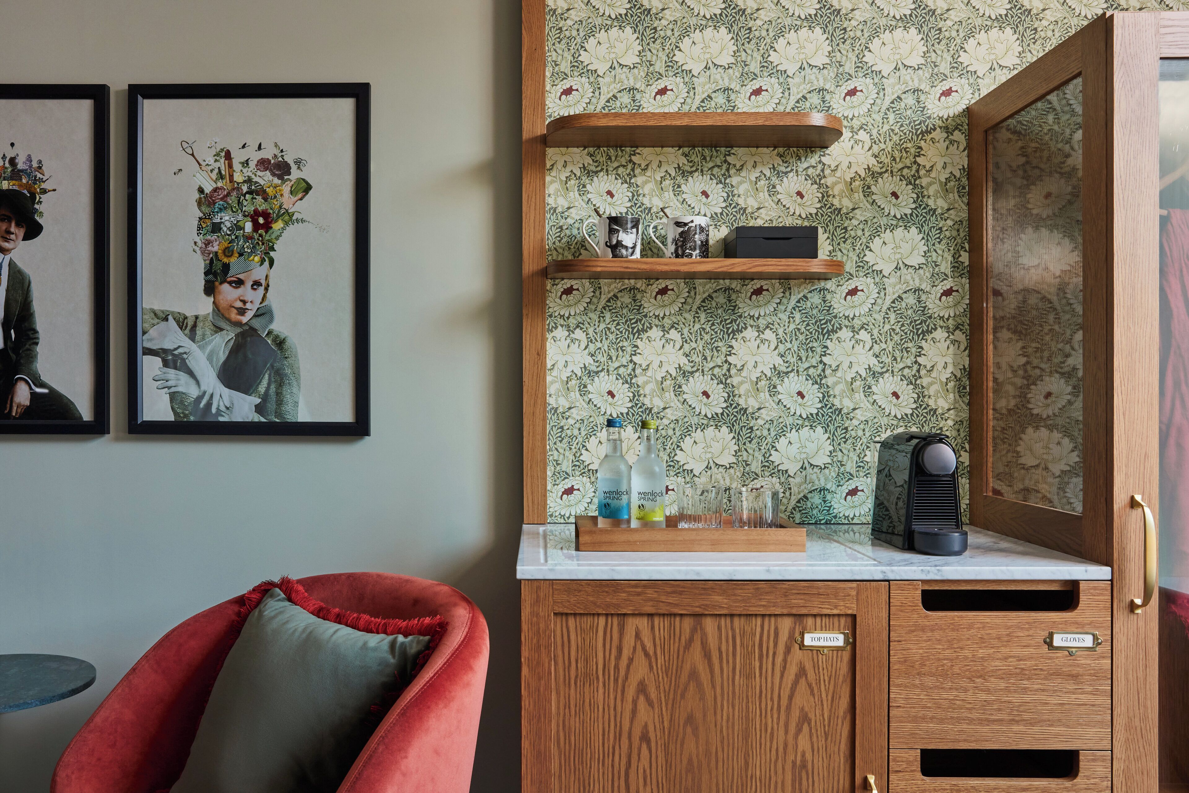 A room with a wooden cabinet, a red chair, and two framed artworks on the wall.