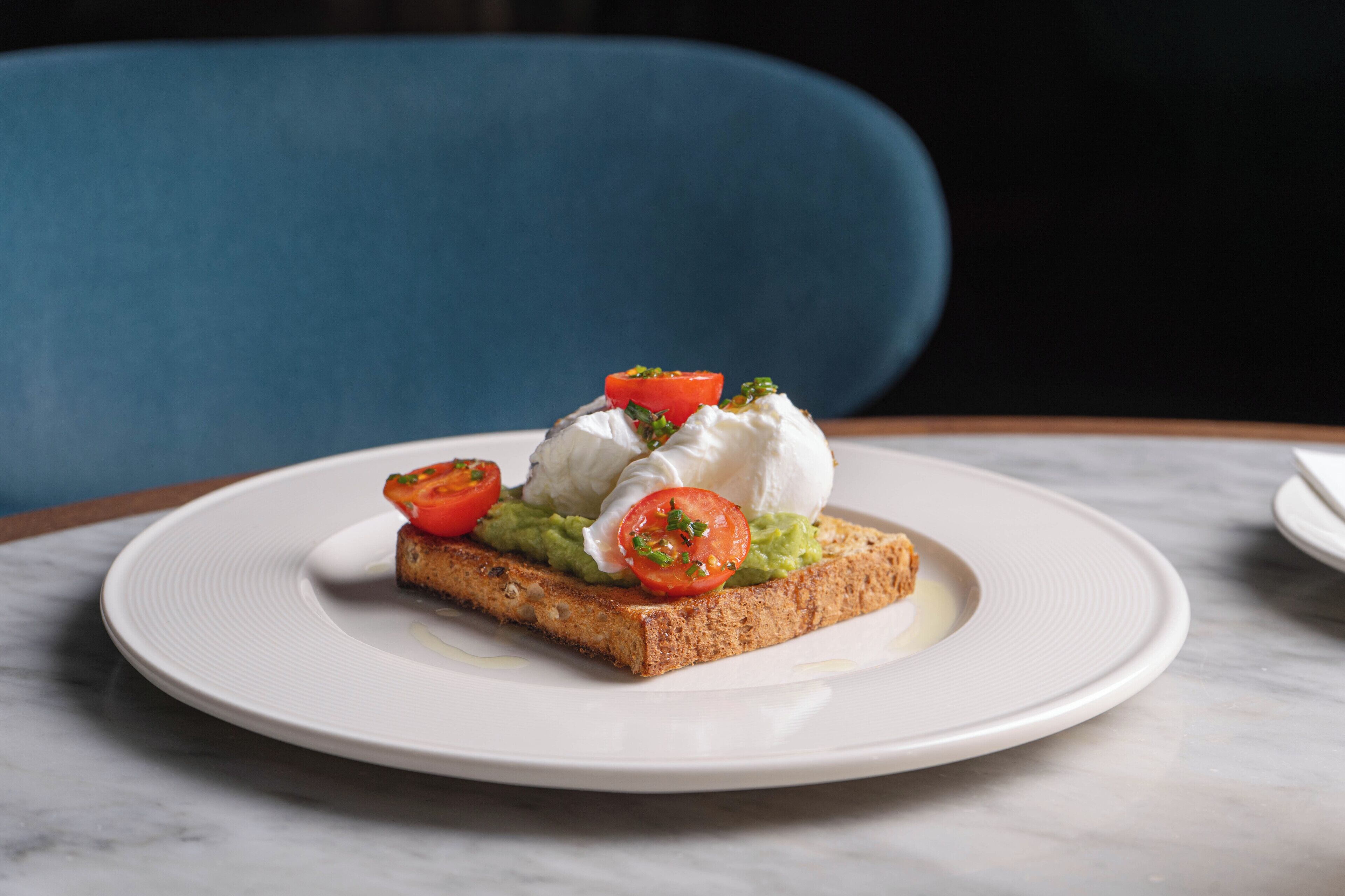 A plate with a slice of toast topped with avocado, tomato, and a dollop of cream cheese.