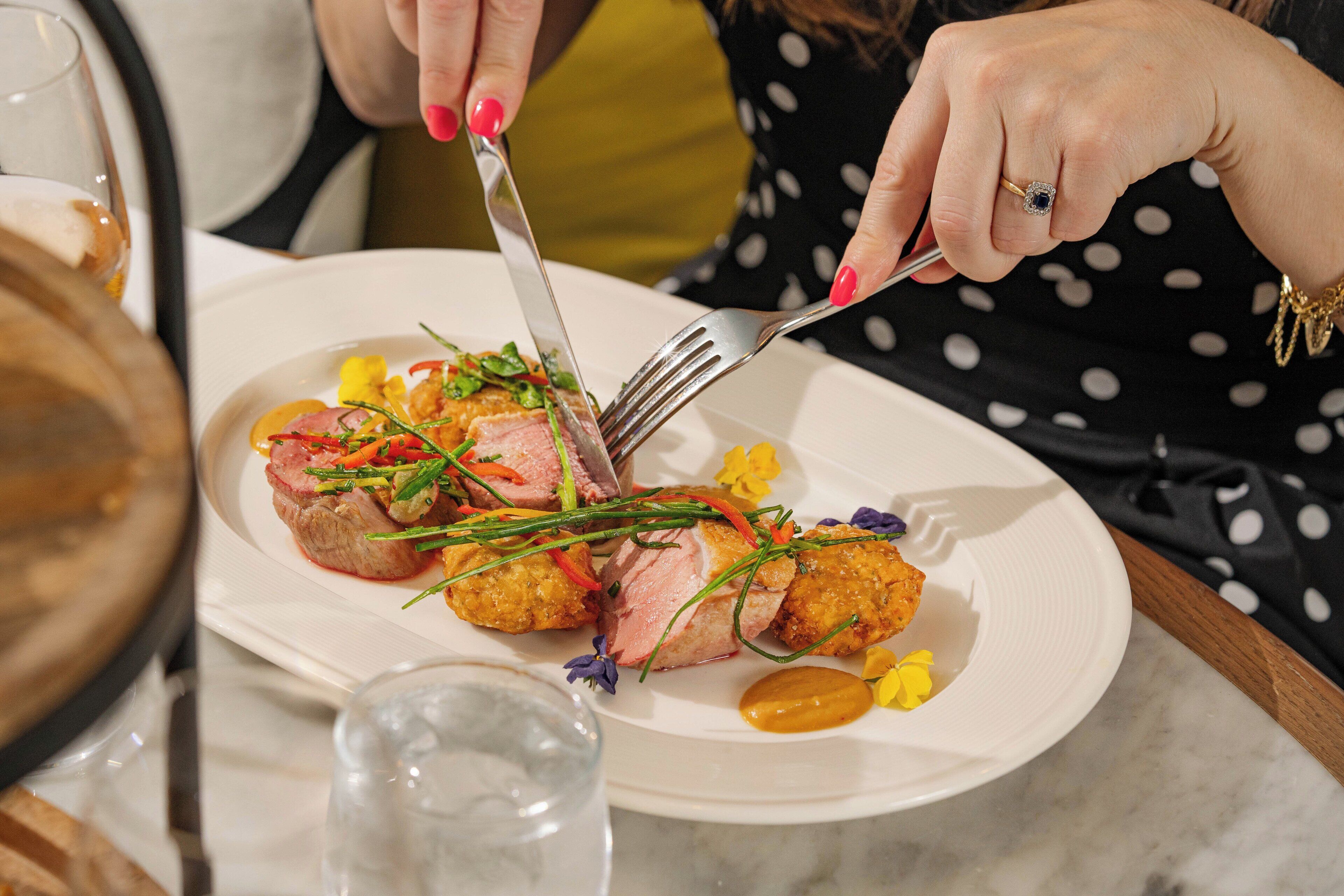 Una persona cortando comida en un plato con un tenedor y un cuchillo.