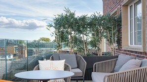 A terrace with wicker furniture, a glass table, and a view of the cityscape.