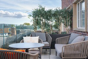 A terrace with wicker furniture, a glass table, and a view of the cityscape.