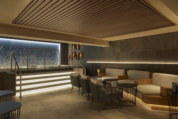 A modern lounge area with a staircase, seating, and a view of the city.