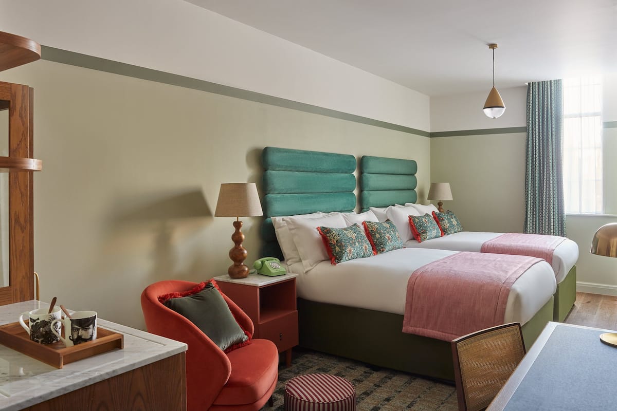 A hotel room with a large bed, a desk with a chair, a nightstand, and a window with curtains.