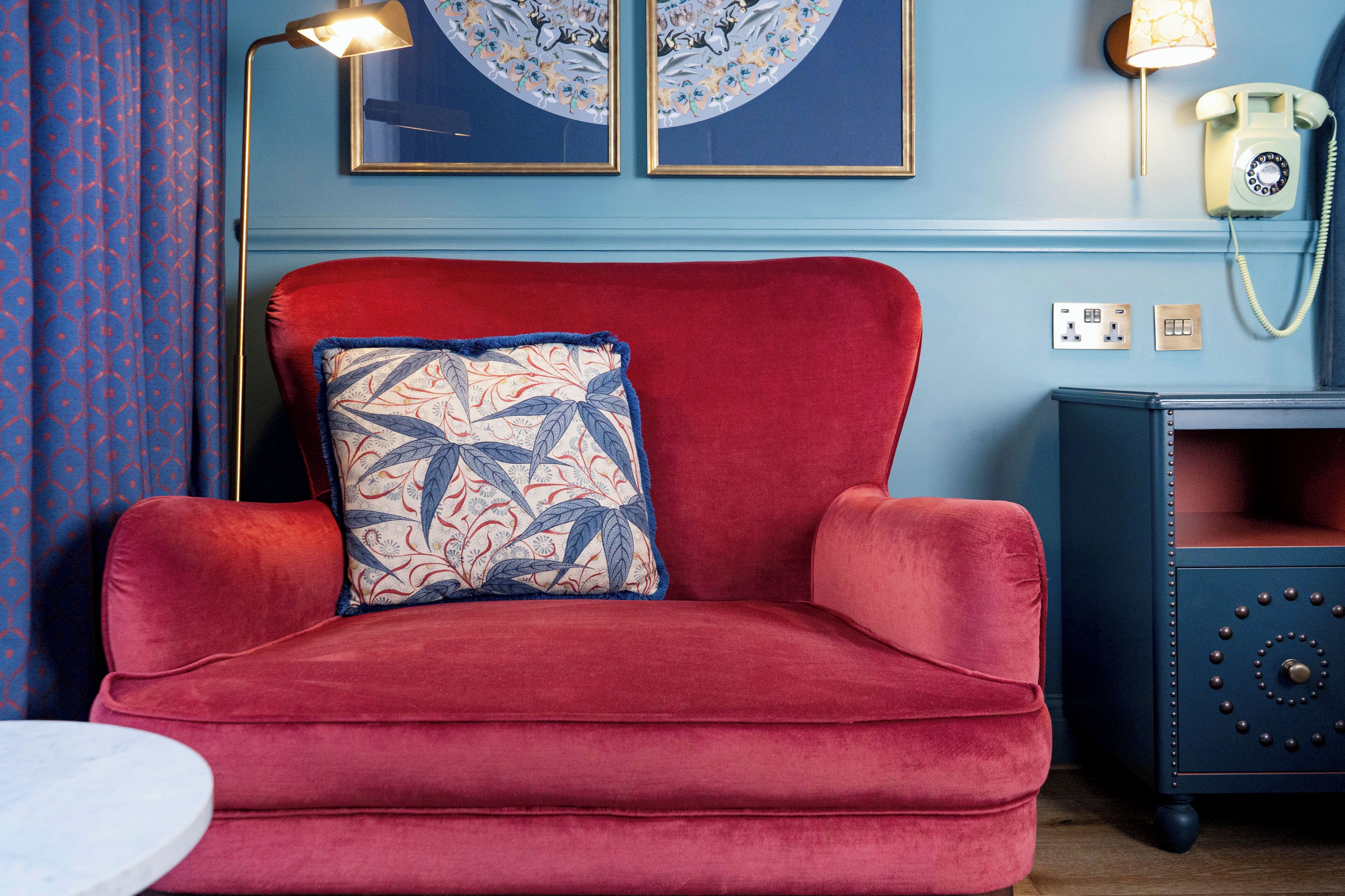 A red velvet sofa with a patterned pillow, a small round table, and a wall-mounted telephone.