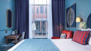 A hotel room with a large bed, a desk, a chair, and a view of a building through a glass door.