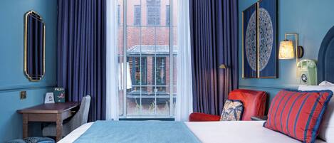 A hotel room with a large bed, a desk, a chair, and a view of a building through a glass door.