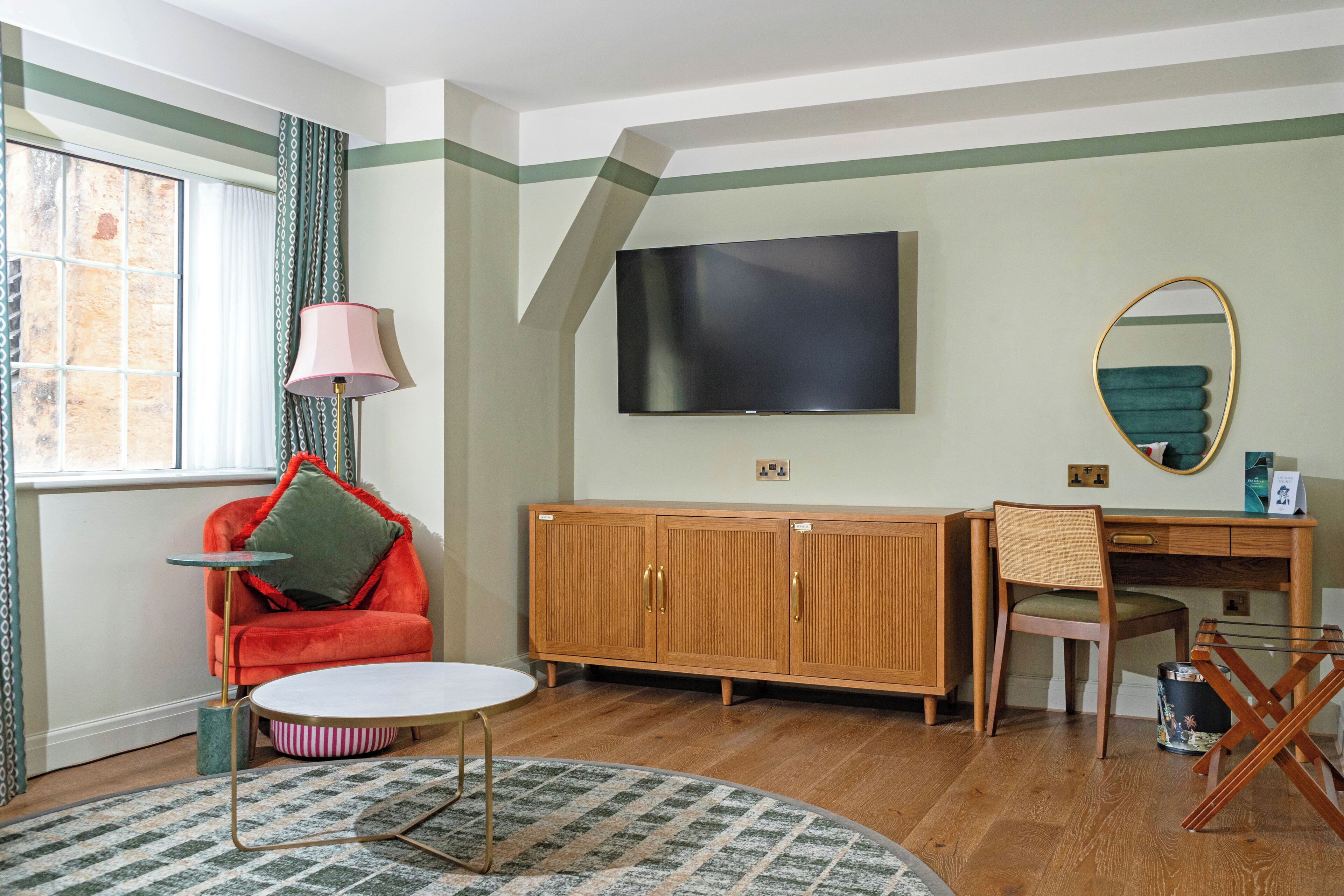 A room with a wooden cabinet, a television, a chair, a desk, and a window with curtains.