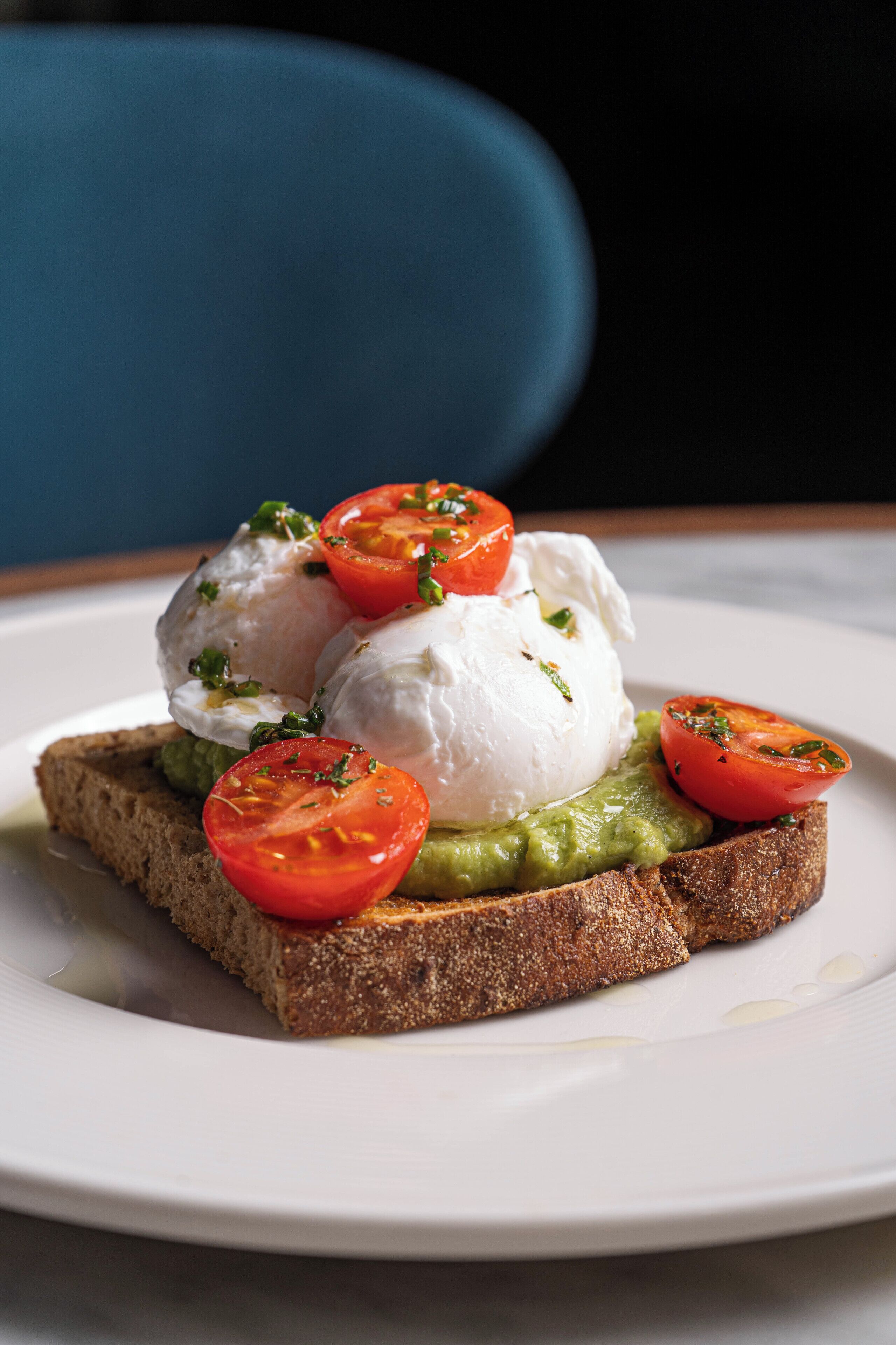 A plate with a slice of bread topped with a creamy spread, a poached egg, and fresh tomato slices.