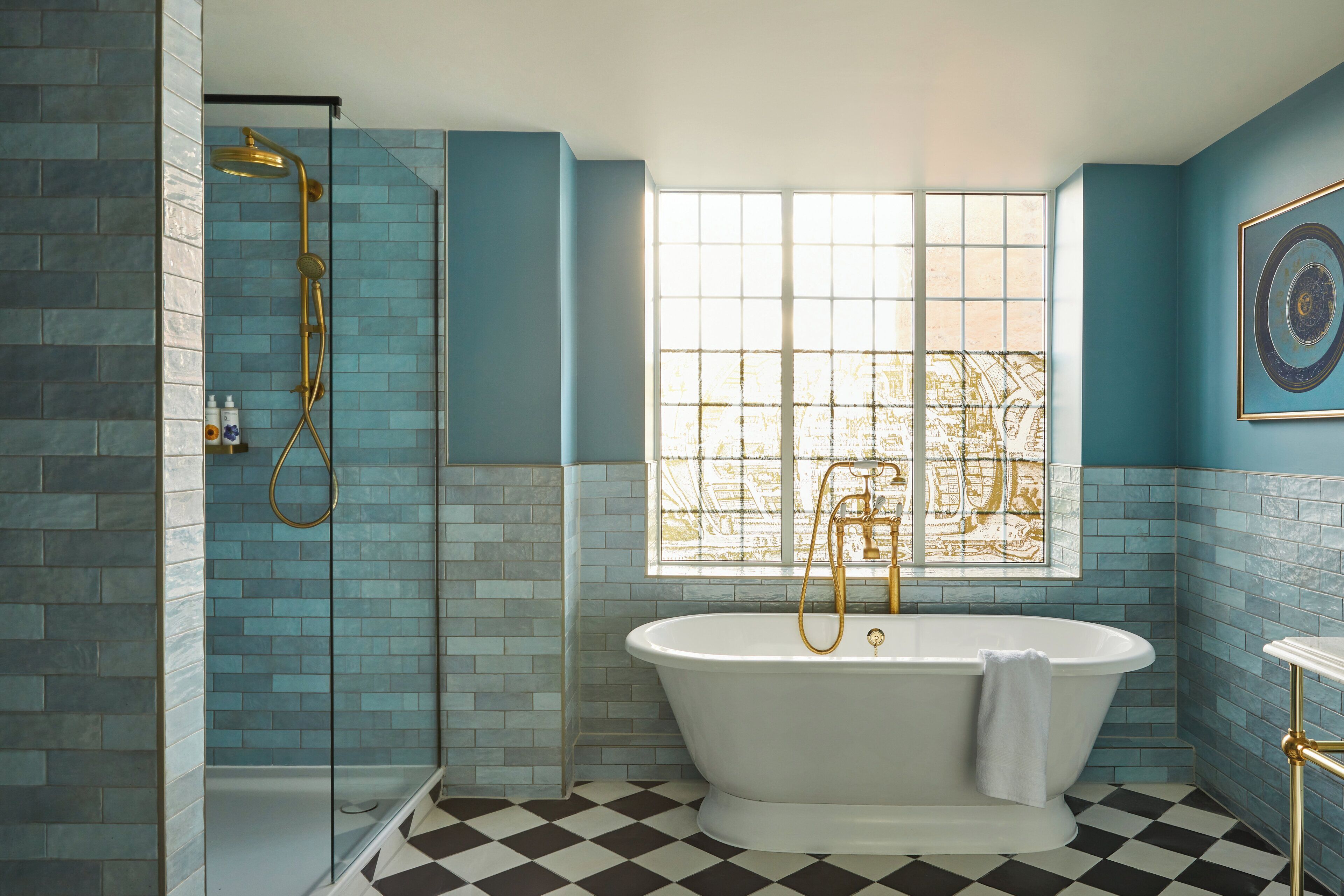 Un baño con una bañera independiente, una ducha con cabezal dorado y una ventana con vista a un paisaje urbano.