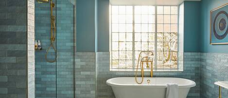 Un baño con una bañera independiente, una ducha con cabezal dorado y una ventana con vista a un paisaje urbano.