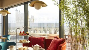 A cafe with a tiered dessert display, a table with cups and a teapot, and a view of a historic tower through large windows. - Hotel Indigo Exeter by IHG (Exeter)