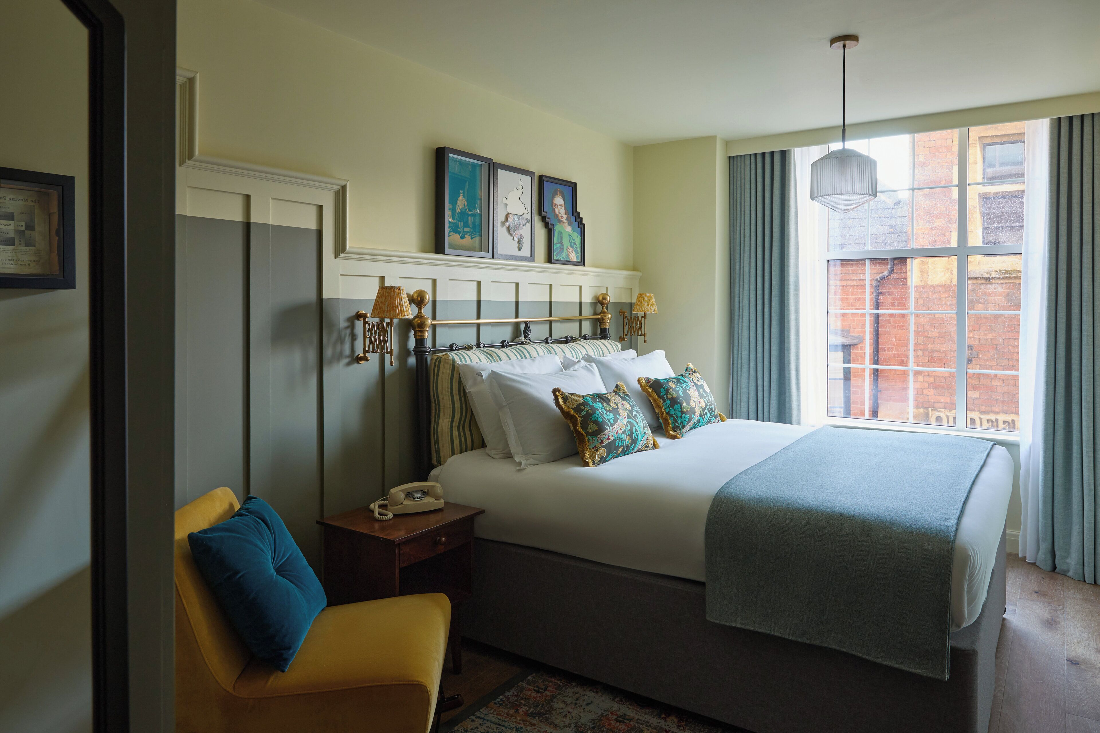 Habitación de hotel con cama, silla, mesita de noche y ventana con vista a un edificio de ladrillo.