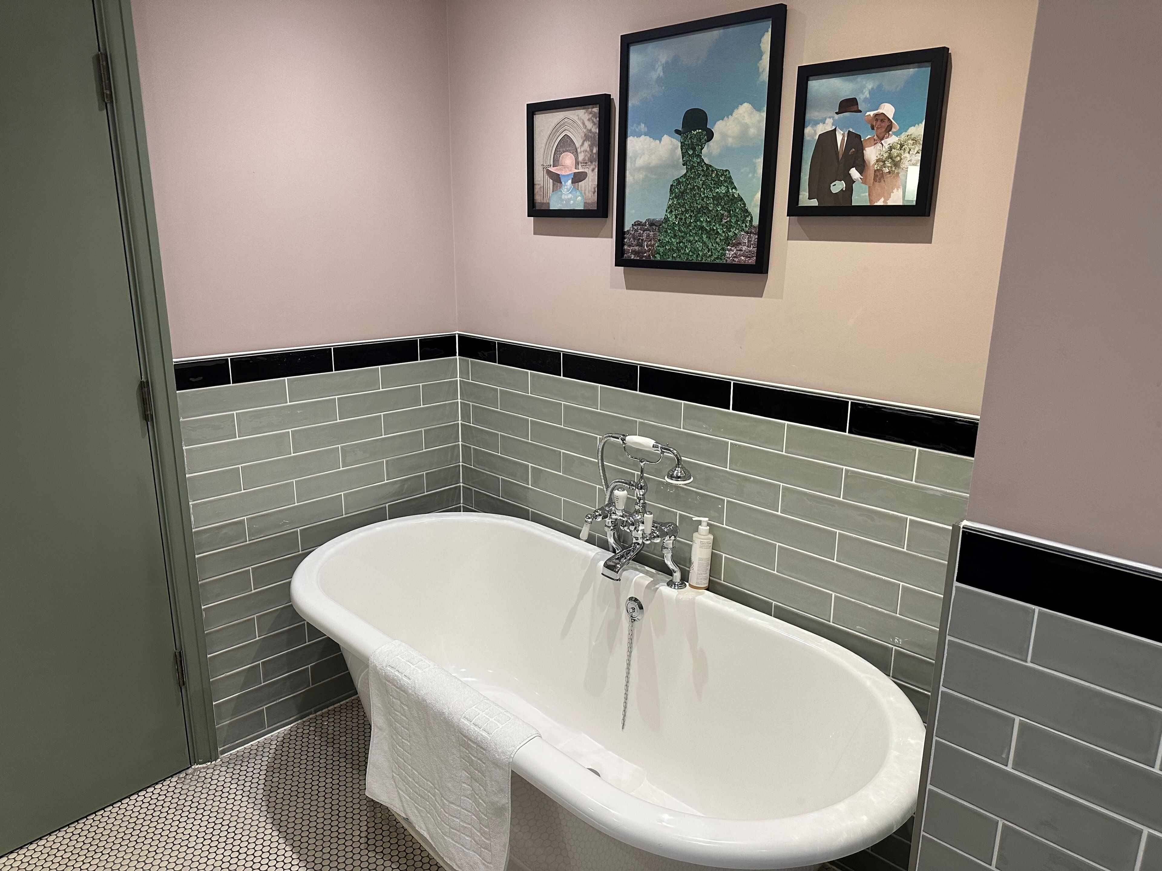 A bathroom with a freestanding bathtub, tiled walls, and three framed artworks on the wall.