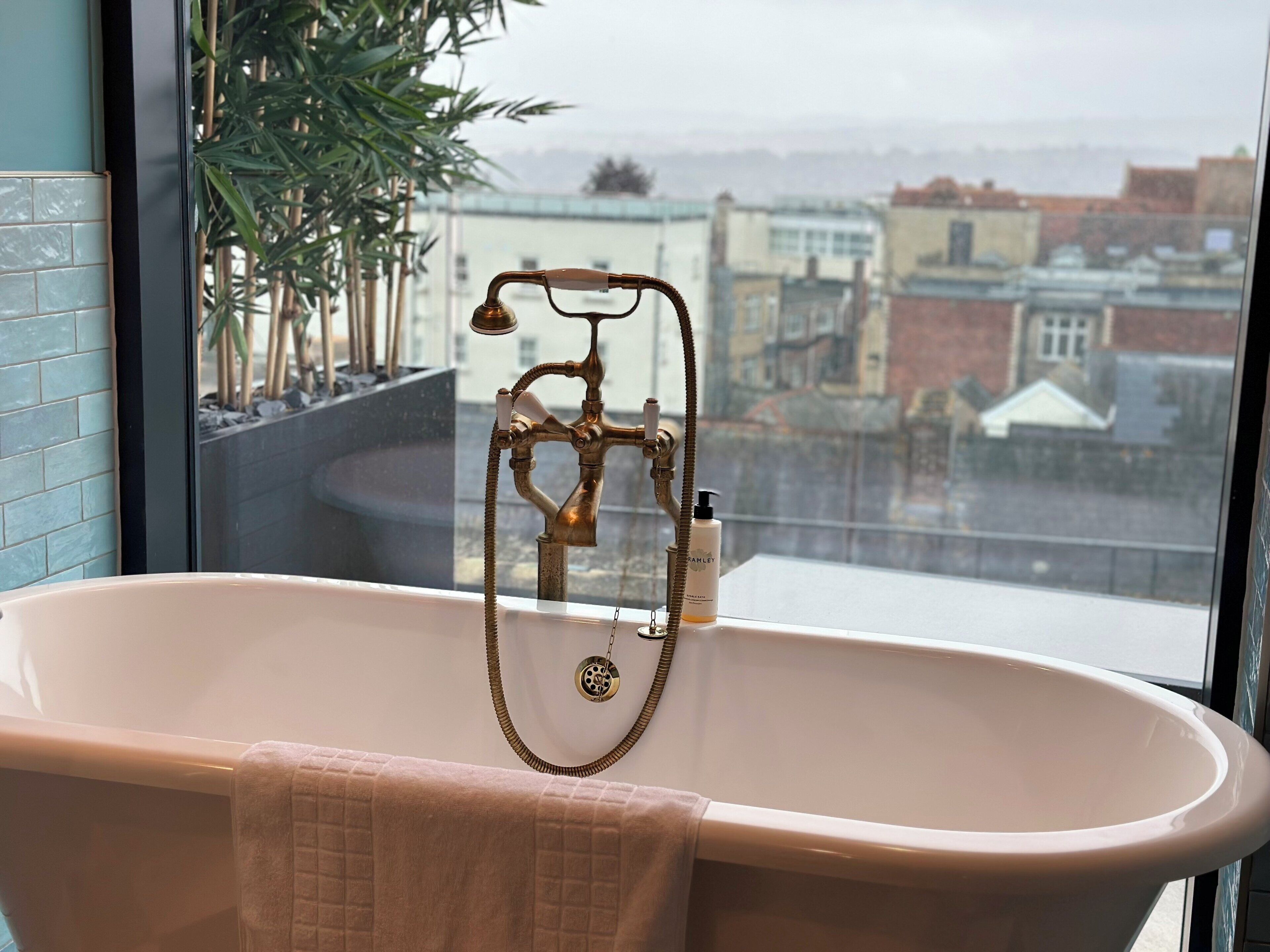 A bathroom with a freestanding bathtub, a towel, and a view of buildings through a window.