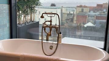 A bathroom with a freestanding bathtub, a towel, and a view of buildings through a window.