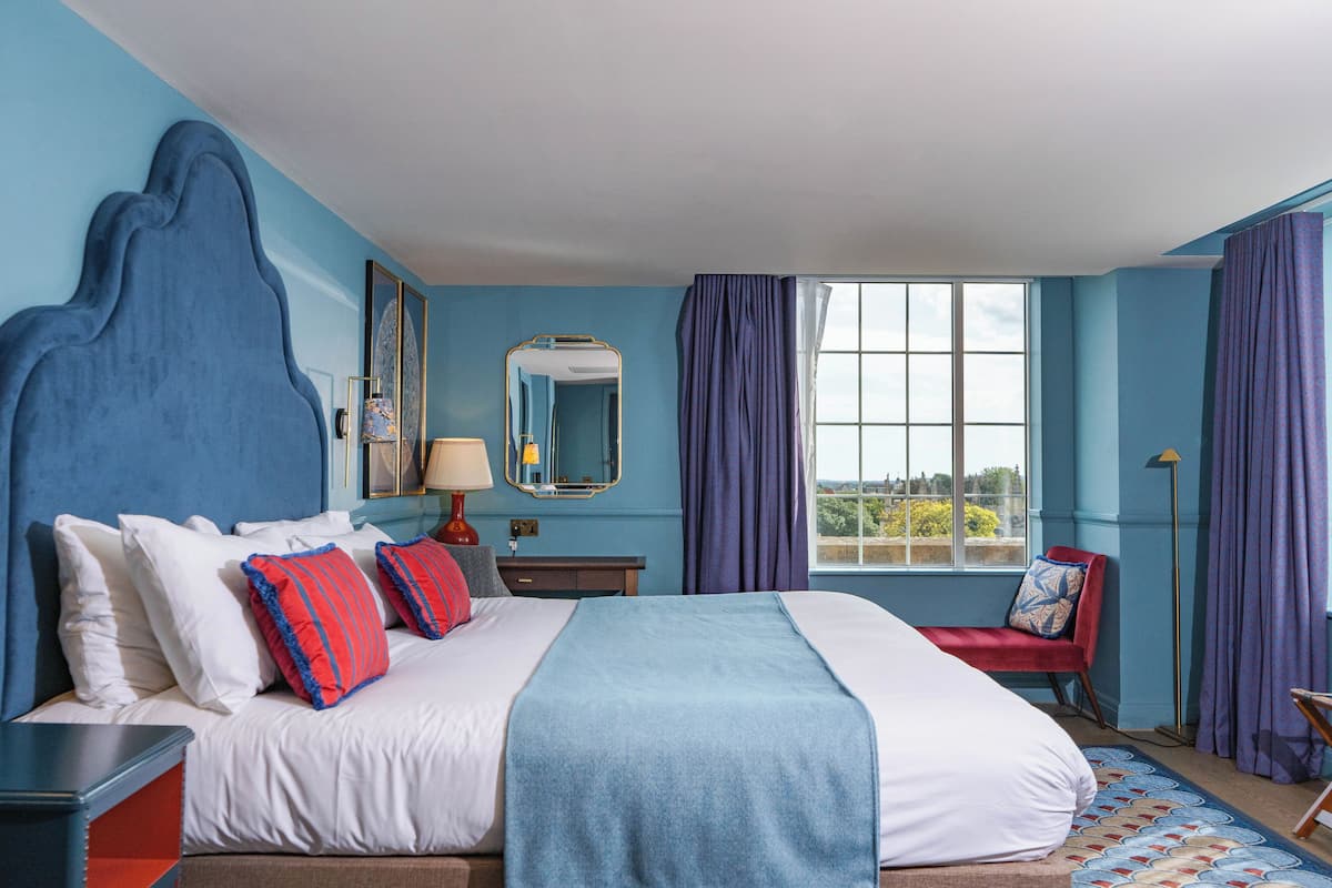 A hotel room with a large bed, a chair, a desk, and a window with curtains.