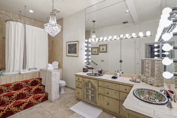 Une salle de bain dotée d’un grand miroir, d’une coiffeuse avec éclairage, d’un lustre et d’un tapis décoratif.