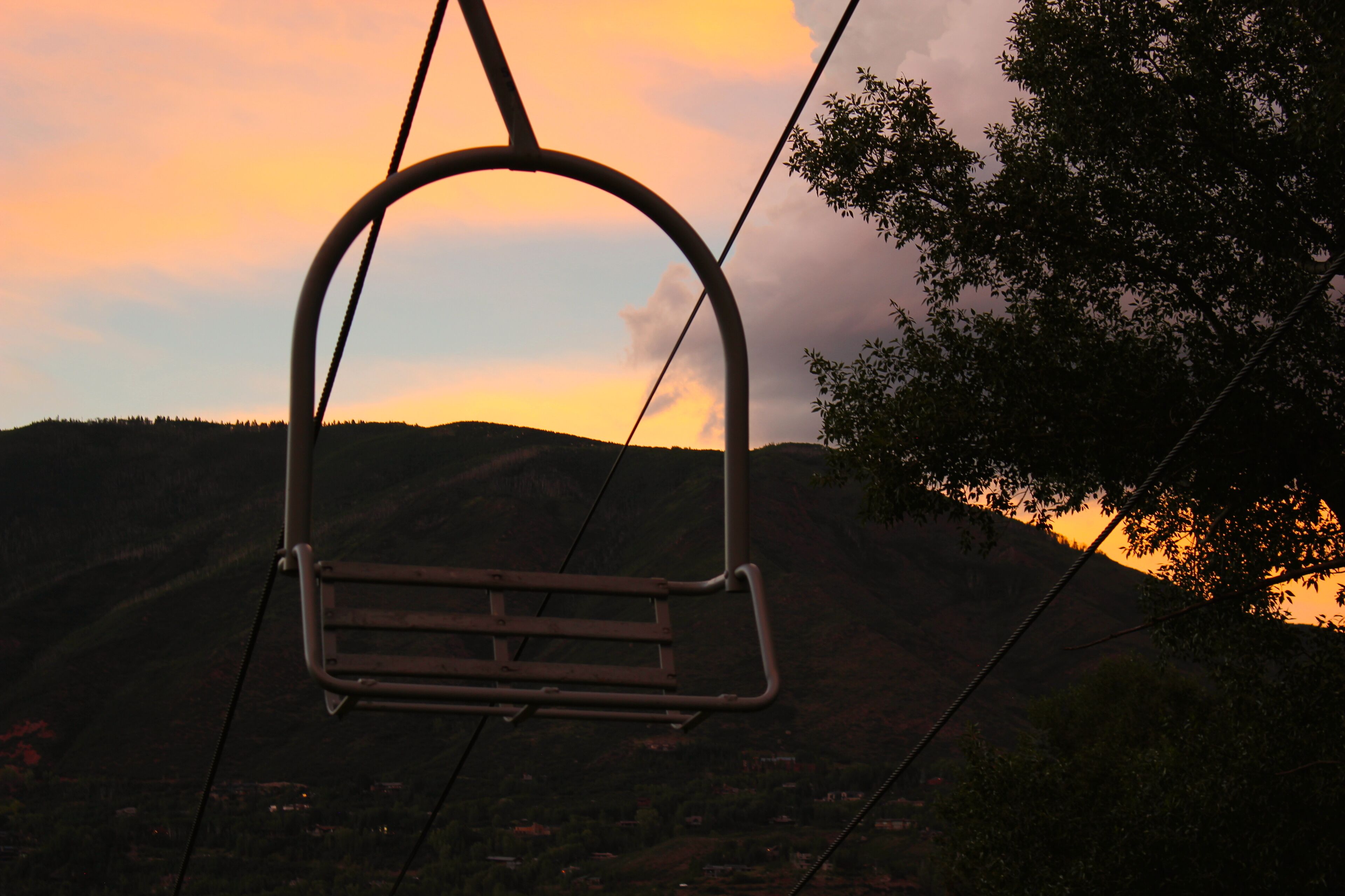 A cable car chair suspended over a mountainous landscape with a sunset in the background.