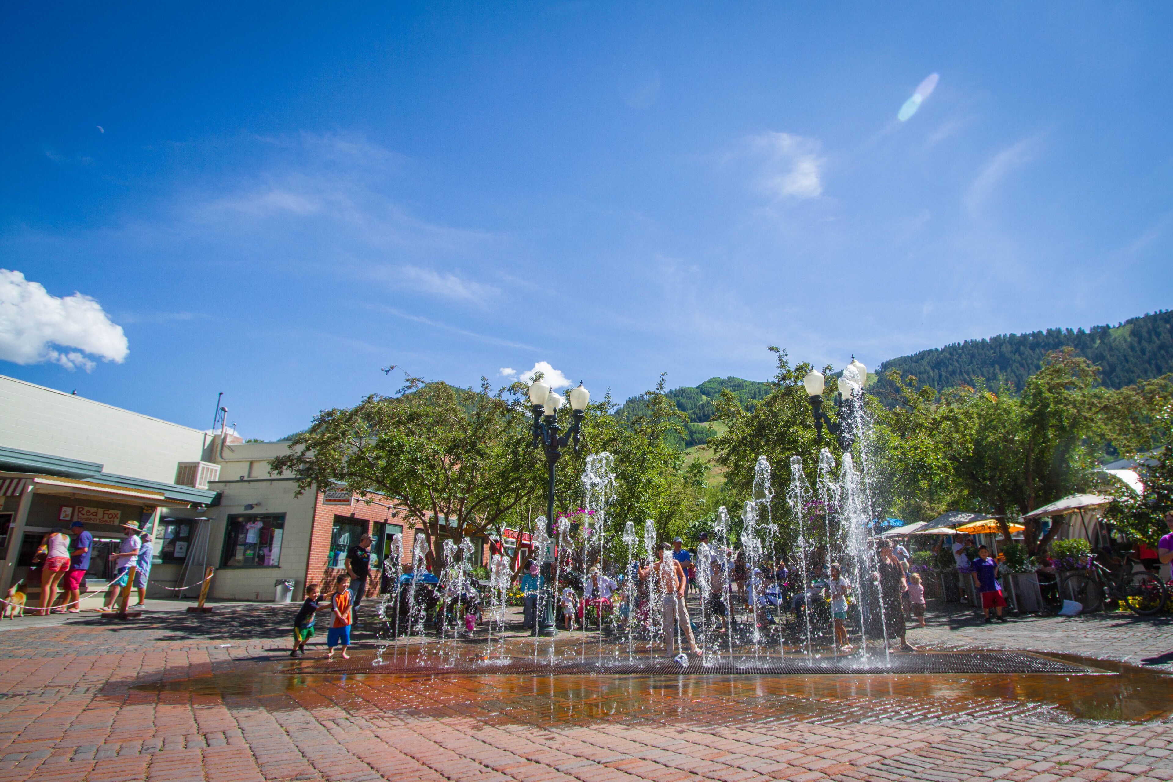 Una plaza pública con una fuente de agua, pavimento de ladrillo y gente.