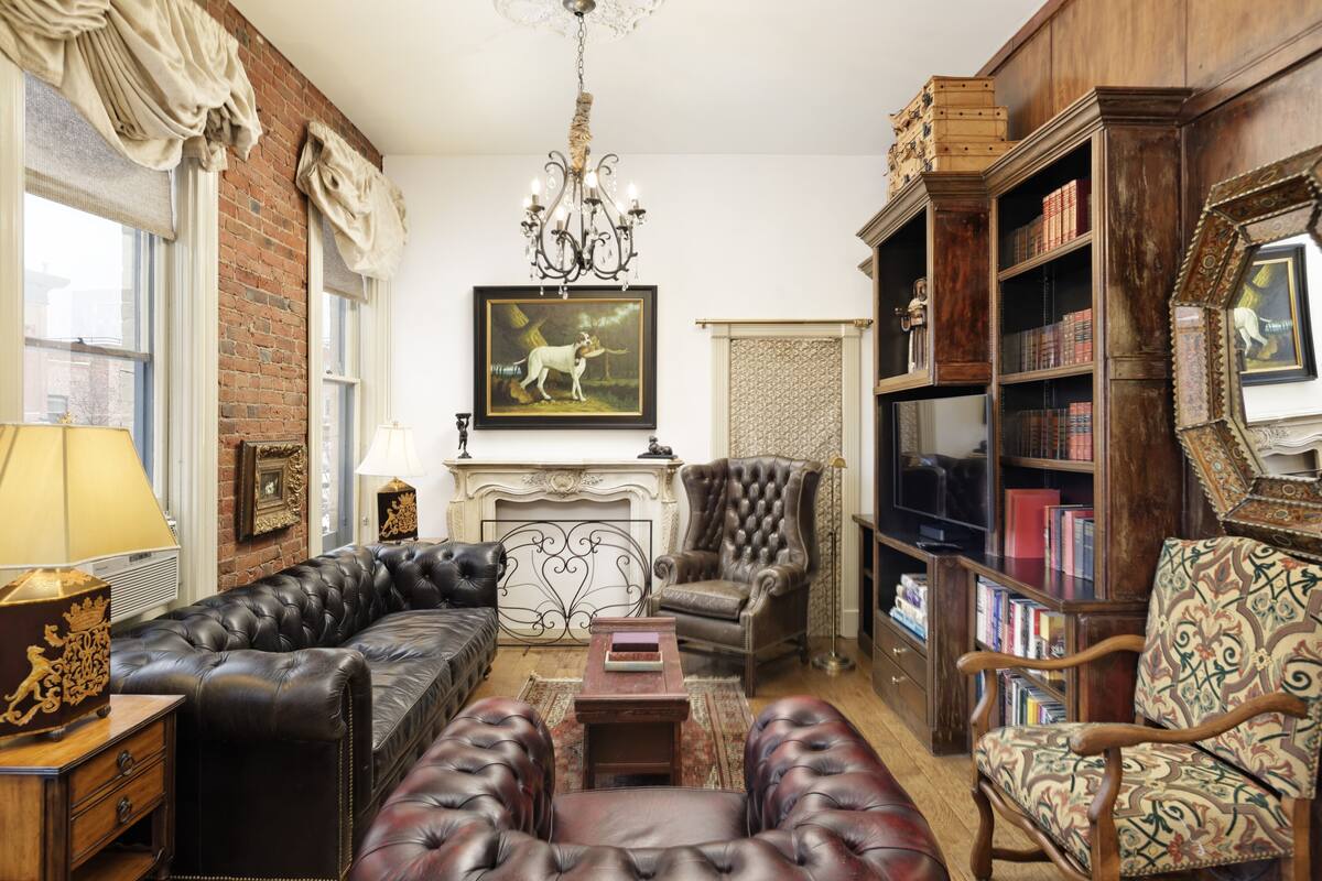 Ein traditionell eingerichtetes Wohnzimmer mit Ledersofas, einem Kamin, Bücherregalen und einer Chandelier.