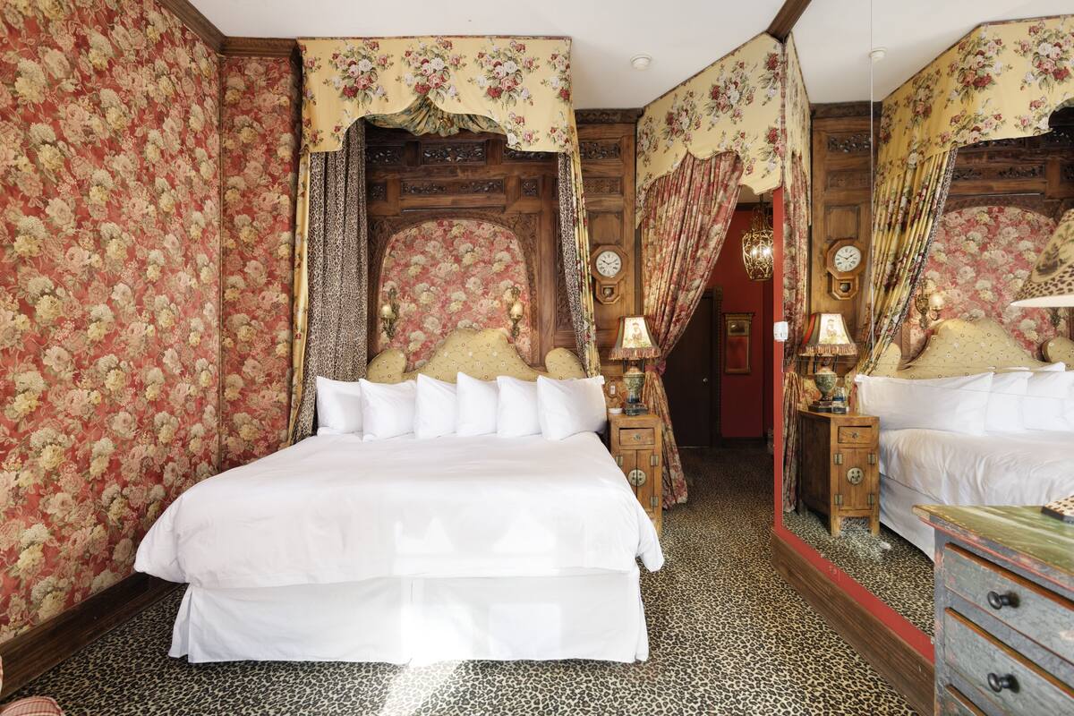 Ein Schlafzimmer mit einem großen Bett, floralem Wandpapier und einem hölzernen Kopfteil.
