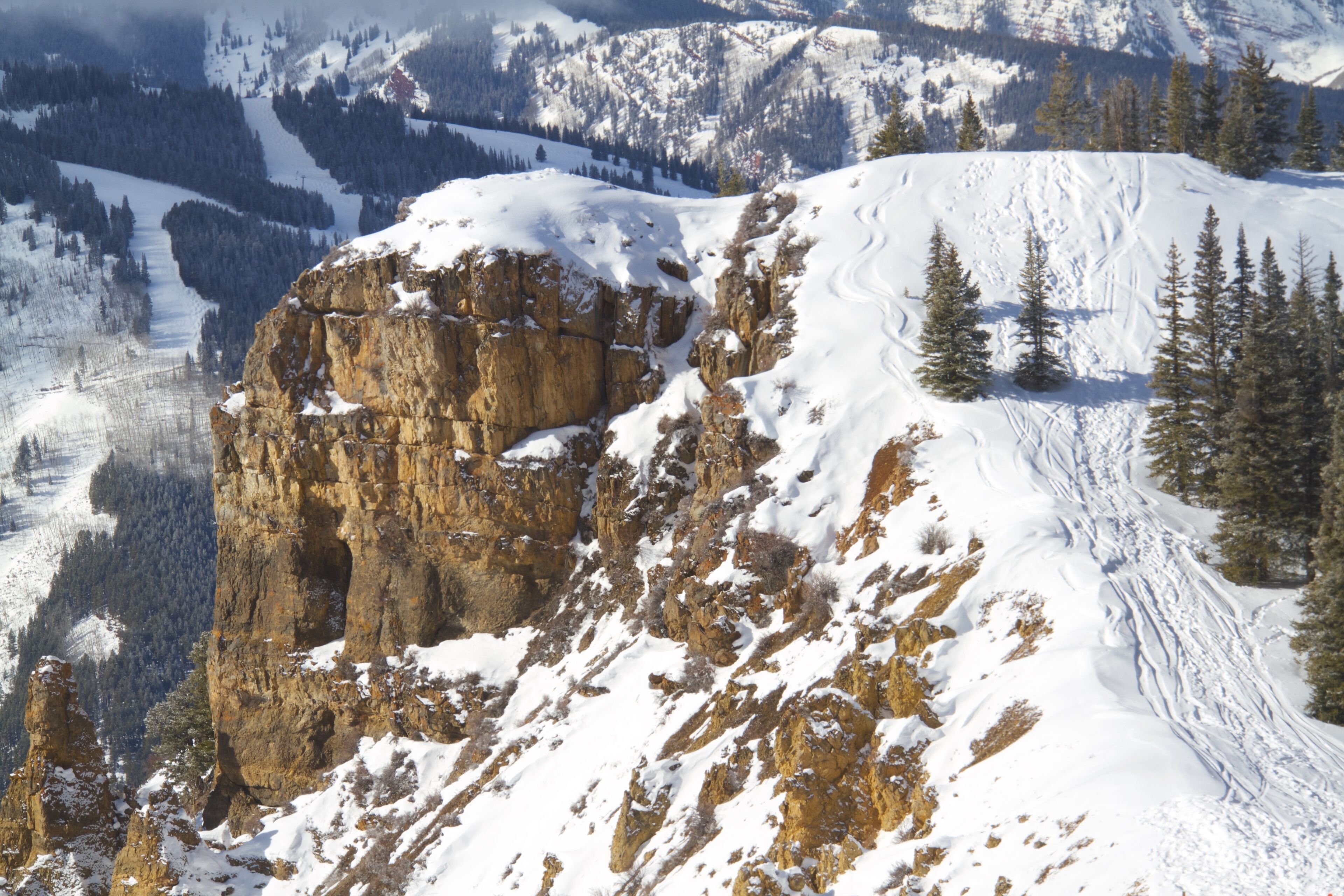 A snow-covered mountain with rocky outcrops and pine trees.